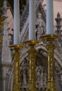 White candles in ornate gold candle holders in foreground with carved marble altar, statues in soft focus background