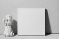 White canvas board and angel figurine against grey wall.