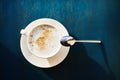 A white cappuccino Cup on a saucer with a teaspoon on a blue table