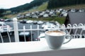 White cappuccino mug on a balcony. Beautiful quiet morning in the mountains. Fresh cup of coffee with foam on a balcony outside. Royalty Free Stock Photo