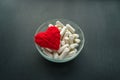 White capsules, tablets in round plate with red thread heart on