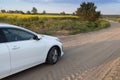 white car drives along a country road among a flowering rapeseed field. forward to adventure