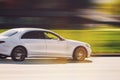 A white car is driving down the street at high speed. Large luxury sedan with motion blur background. Abstract photography of a Royalty Free Stock Photo