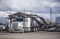 White car hauler big rig semi truck with empty modular semi trailer standing on the industrial parking lot with another trucks