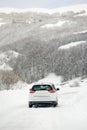 White car riding on a snow-covered road in the European Alps while a snowstorm. Drifts and snow drifts during a snowfall Royalty Free Stock Photo