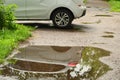 The back of a white passenger car parked at the edge of the road is reflected in a puddle on the sidewalk after rain Royalty Free Stock Photo