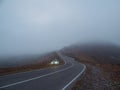 A Range Rover car SUV with fog lights turned on is parked next to scenic route road in a foggy autumn landscape. Luggage trunk box
