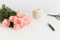 White card, bouquet of pink roses and a twine on a white table