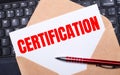 White card with the text CERTIFICATION in a craft envelope on a work desk with a modern laptop keyboard and burgundy pen. Flat Royalty Free Stock Photo