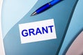 White card with text GRANT and a blue pen on a blue, blue and pink background