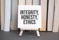 White card with text INTEGRITY, HONESTY, ETHICS stands on the desk against the background of books stacked