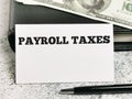 White card with text PAYROLL TAXES with a pen and fake money.