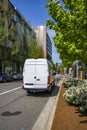 White cargo mini van with high roof making delivery driving on the modern city street with sun and shadow Royalty Free Stock Photo