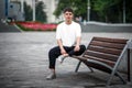 White casual t-shirt mockup on a guy sitting against a blurred park background on a bench front view for design presentation 