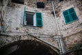 White cat sitting high on window sill, open green windows and old medieval stone wall