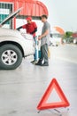 White caucasian car owner and Asian gas station worker man checking auto car engine behind traffic sign after filling high energy