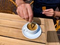 White caucasian male hand stirs a freshly brewed cup of coffee on a patio terrace on a wooden table