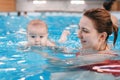 Mother traning her newborn baby to float in swimming pool