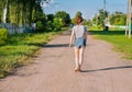 White Caucasian young girl on a sunny summer day walks along a dirt road in the countryside and admires nature, the view from the Royalty Free Stock Photo