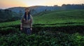 A white Caucasian young smiling woman with blue pigtails stands at sunset on a field with flowering bushes of tea.