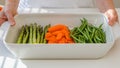 White ceramic baking dish, and fresh vegetables, carrot, green beans, asparagus. close up on white kitchen table. Cooking process Royalty Free Stock Photo