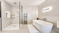 White ceramic bathtub placed near glass shower cabin in stylish spacious bathroom with heated towel rail and bright glowing lamps Royalty Free Stock Photo