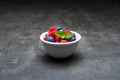 White ceramic bowl with berry fruit, water drops on blueberries and raspberries with mint leaves on dark concrete background. Royalty Free Stock Photo