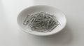 A white ceramic bowl contains a pile of metallic paperclips. The paperclips are silver- Royalty Free Stock Photo