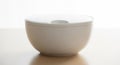 White ceramic bowl with a matching lid sits on a light wooden surface. The bowl has a smooth Royalty Free Stock Photo
