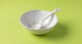 White ceramic bowl with a matching spoon inside, placed on a light green surface. Royalty Free Stock Photo