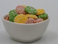 White ceramic bowl of pastel colored white chocolate mints coated with white sprinkles on a clean background