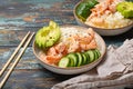 White ceramic bowl with rice, shrimps, avocado, vegetables and sesame seeds and chopsticks on colourful rustic wooden Royalty Free Stock Photo