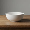A white ceramic bowl with a smooth surface sits on a wooden table. The table\'s surfa Royalty Free Stock Photo