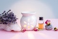 White ceramic candle aroma oil lamp with essential oil bottle and dried flowers, crystal geodes on modern pastel pink and blue bac