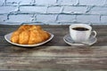 White ceramic cup with black coffee, a spoon and a plate with two fresh croissants Royalty Free Stock Photo