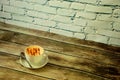 A white ceramic cup of cappuccino with white foam and a sprinkle of cinnamon is in a saucer with a spoon on a wooden table on an Royalty Free Stock Photo