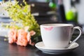 White ceramic cup of coffee with lipstick traces on black laptop desk with Artificial Flowers and magazines background. selective Royalty Free Stock Photo