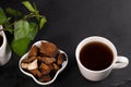 White ceramic cup of healing infusion of birch mushroom chaga, bowl with chaga pieces and birch leaves on black