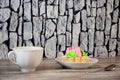 A white ceramic cup with a hot drink and a shortbread basket with multi-colored cream are on the table against the wall