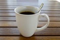 A white ceramic cup with a morning refreshing hot coffee with tea drink and tea shiny teaspoon is on a wooden table in a cafe Royalty Free Stock Photo