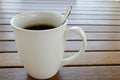 A white ceramic cup with a morning refreshing hot coffee with tea drink and tea shiny teaspoon is on a wooden table in a cafe Royalty Free Stock Photo