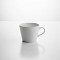 White ceramic cup on a smooth, reflective surface, set against a plain white background. Royalty Free Stock Photo