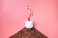 A white ceramic cup stands on a hill of coffee beans on a pink background