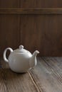 White ceramic mockup teapot for hot tea on empty old wooden table near wall made of brown timber planks. Vertical banner