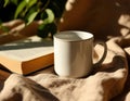 White ceramic mug and book on fabric with sunlight creating soft spots and shadows. Royalty Free Stock Photo