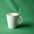 A white ceramic mug with a curved handle sits on a smooth green Royalty Free Stock Photo