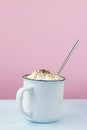 White ceramic mug filled with hot chocolate with whipped cream and cocoa powder sprinkled on top with a metallic straw on a pink