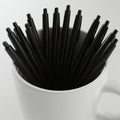 A white ceramic mug filled with multiple black click pens, arranged with the tips facin Royalty Free Stock Photo
