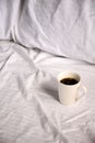 White ceramic mug with freshly brewed coffee atop a bed of crisp, white sheets Royalty Free Stock Photo