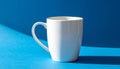 White Ceramic Mug with Handle on Blue Surface with Dramatic Shadows white mug blue background Royalty Free Stock Photo
